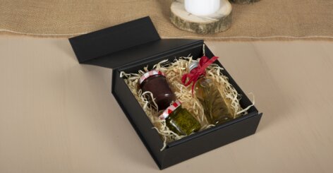 Darstellung der flachen Geschenkbox  im geschlossenen Zustand mit Geschenkbeispiel, einer kleinen Weinflasche und Pesto im Glas.