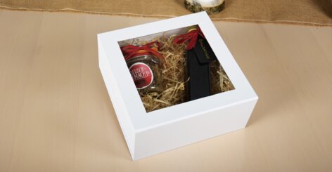 Darstellung der Geschenkbox mit Fenster im geschlossenen Zustand mit Geschenkbeispiel, einer kleinen Weinflasche und Pesto im Glas.